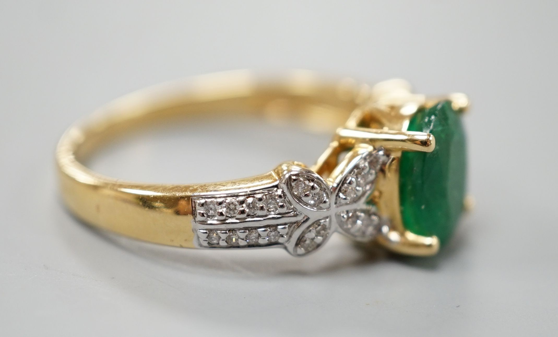 A modern 18ct gold and single stone emerald set dress ring, with diamond chip set shoulders, size R, gross weight 5.5 grams.
